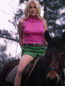 Blonde female reveals thigh and ass while mounting her horse in a short skirt