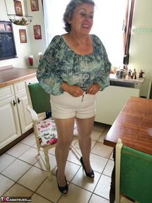 Old woman Caro pulls down her pantyhose in high heels at kitchen table